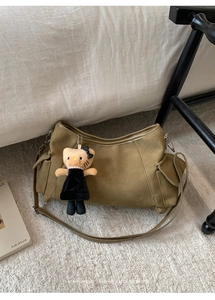 Olive green retro suede shoulder bag with plush pendant on a soft white carpet background