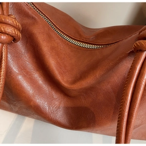 Close-up of brown soft leather tote bag featuring a knotted strap and golden zipper detail