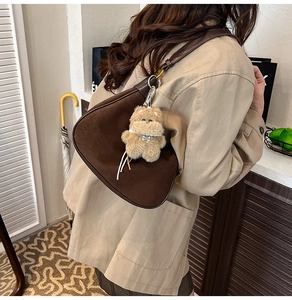 Detail of dark brown suede hobo bag with teddy bear charm on model shoulder