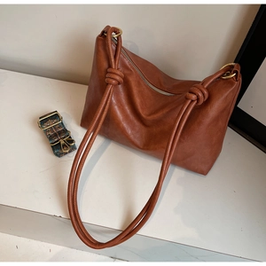 Close-up of brown tote bag with textured finish, knot handle and colorful woven strap