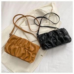 Detail of pleated PU leather crossbody bags in black and tan on a white blazer
