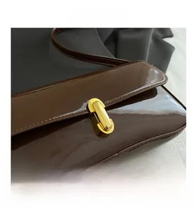 Close-up of golden capsule lock on brown patent leather underarm bag detail