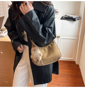 Detail of a brown suede hobo bag with cute bear charm worn by a model in casual style