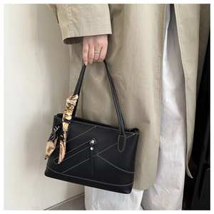 Detail of a black leather tote bag with white contrast stitching and a silk scarf handle