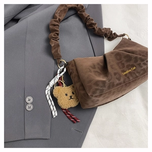 Detail of brown leopard embossed ruched underarm bag with a plush bear charm on a blazer