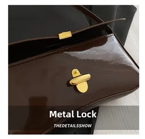 Detailed close-up of high-shine brown patent leather and golden hardware clasp on baguette bag