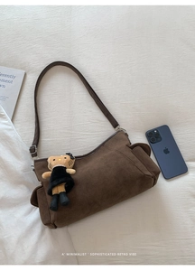 Detail view of brown matte suede shoulder bag with plush doll charm on white fabric