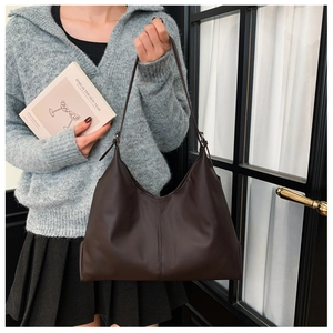 Detail of a large dark brown leather tote bag with a matte finish and slender straps