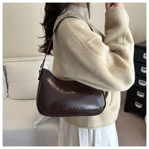 Detail of dark brown leather underarm bag featuring a minimalist crescent design and smooth texture