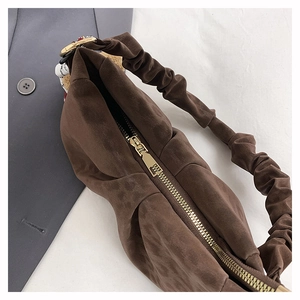 Detail of coffee brown suede handbag featuring a ruched handle and smooth gold zipper