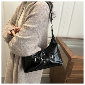 Detail of black patent leather underarm bag featuring silver rivets and metal buckle hardware