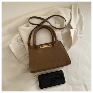 Close-up of vintage brown matte leather handbag with golden twist lock on a beige blazer