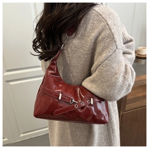 Detail of burgundy patent leather underarm bag with silver metallic hardware worn by model