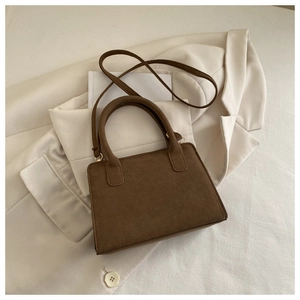 Detailed top view of a dark brown matte suede handbag on a beige blazer background