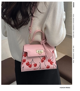 Close-up of pink cherry print tote bag featuring a gold twist lock and a slim strap