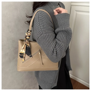 Detail of khaki leather tote with diagonal zipper and decorative patterned silk scarf