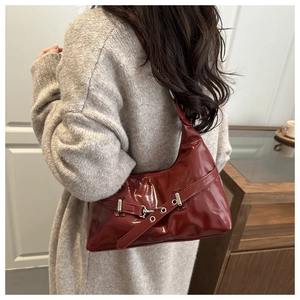Detail of dark red glossy underarm bag with silver buckle worn by a model in a cozy setting