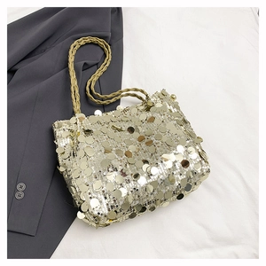 Detail of a gold sequined tote bag featuring a woven strap on a white fabric background