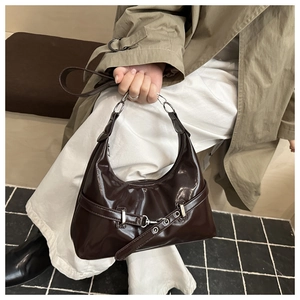 Close-up of a dark brown patent leather half-moon shoulder bag with metal buckle detail