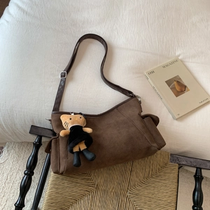 Vintage dark brown frosted crossbody bag with cat plush charm on a cozy bed background