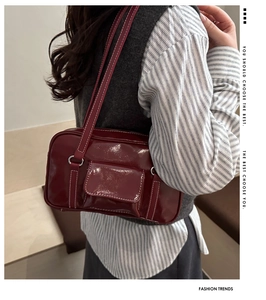 Detail of dark red glossy shoulder bag with white contrast stitching and front pocket