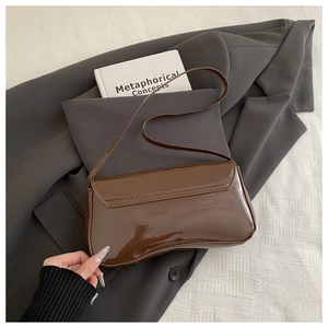 Top-down view of a vintage brown patent leather underarm bag on a grey blazer fabric