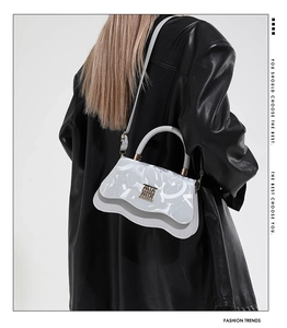 Detail of white leather handbag featuring wavy flap and golden logo on a black jacket
