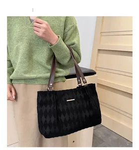 Dettaglio della trama in velluto trapuntato nero e tracolla marrone della borsa tote