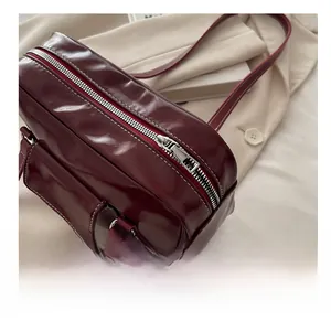 Detail of burgundy glossy leather shoulder bag with white contrast stitching and silver zipper