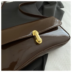 Close-up of brown patent leather shoulder bag with a gold cylindrical turn-lock buckle