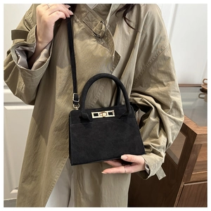 Dettaglio di una borsa a tracolla nera opaca con finiture dorate indossata da una modella