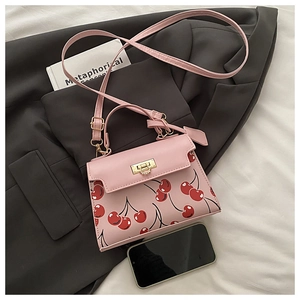 Sac bandoulière rose imprimé cerises, fermoir doré et poignée sur une veste grise
