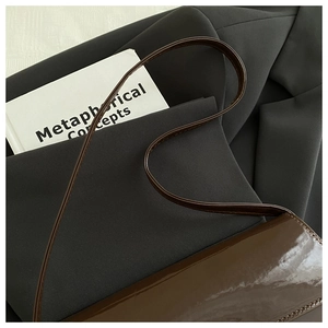Detail view of dark brown patent leather shoulder bag with sleek mirror finish on blazer