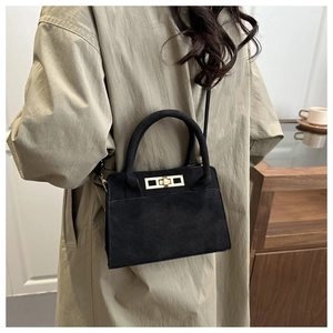 Detail of black suede trapezoid handbag with gold twist lock and circular top handle