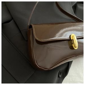 Close-up of brown patent leather baguette bag with shiny finish and gold metal clasp
