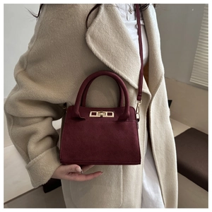 Détail du sac à main bordeaux en cuir givré avec fermoir doré sur manteau en laine