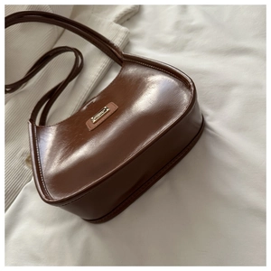 Détail d'un sac porté épaule en cuir ciré marron foncé avec logo en métal sur tissu blanc