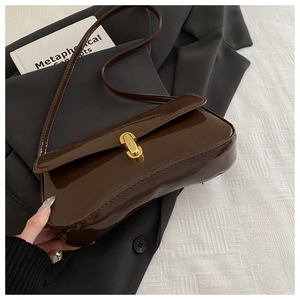 Detail of a brown patent leather shoulder bag with a gold metal clasp on a grey blazer
