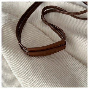 Détail de bandoulières en cuir marron avec coutures renforcées sur surface en velours blanc