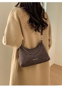 Dettaglio della borsa a mezzaluna marrone scuro con catena indossata su cappotto kaki