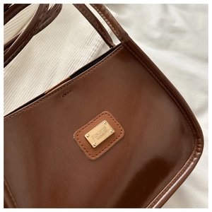 Gros plan sur la texture du cuir poli marron et la plaque logo dorée du sac à main
