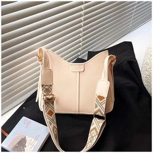 Minimalist beige leather shoulder bag with wide geometric strap on a black blazer