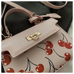Détail d'un sac rose avec imprimé cerise et fermoir rotatif en métal doré