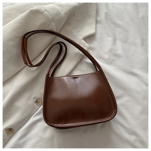 Close-up of brown polished leather shoulder bag placed on cream knitted cardigan and fabric