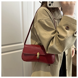 Close-up of red patent leather baguette bag with unique gold metal buckle and flap