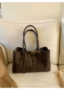 Detailed close-up of dark brown leather tote bag with gold buckle on a beige sofa