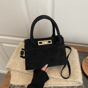 Retro black matte handbag with gold square lock and shoulder strap on beige fabric