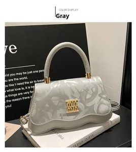 Detail of grey crossbody bag with wavy edge design and abstract embossed letter pattern