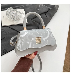 Detail of grey handbag with wavy flap and golden metallic logo on premium leather