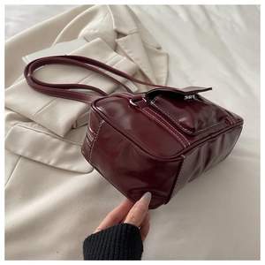 Detail of burgundy glossy shoulder bag with white contrast stitching and vintage front pocket